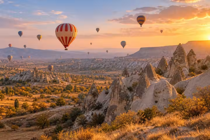 Hot air balloons floating above sunlit Cappadocia valleys and fairy chimneys