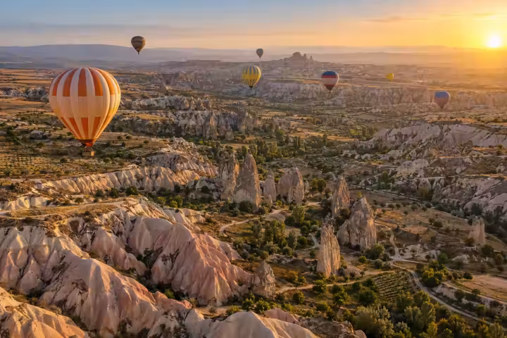 Orange hot air balloon floating above Cappadocia’s valleys at sunrise