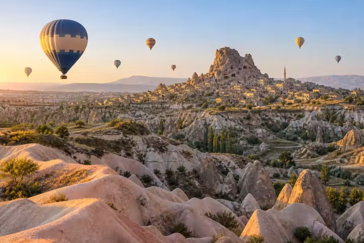Blue hot air balloon above Cappadocia’s valleys near Uchisar Castle at sunrise