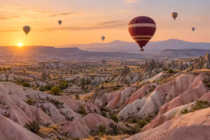 Burgundy hot air balloon above Cappadocia’s pink valley ridges at sunrise