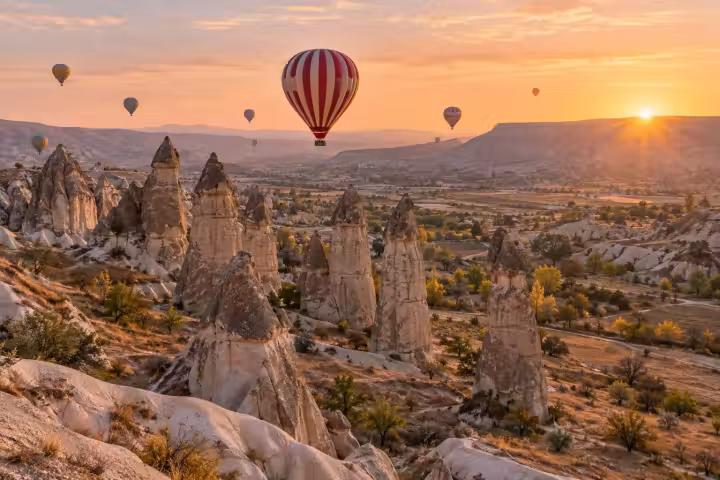 Red and cream hot air balloon above Cappadocia fairy chimneys at sunrise