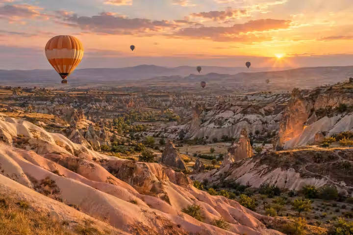 Orange and ivory balloon above Cappadocia’s rose-coloured valleys in golden sunrise light