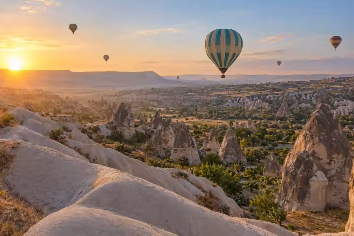 Teal and cream hot air balloon over Cappadocia’s pale rock ridges at sunrise