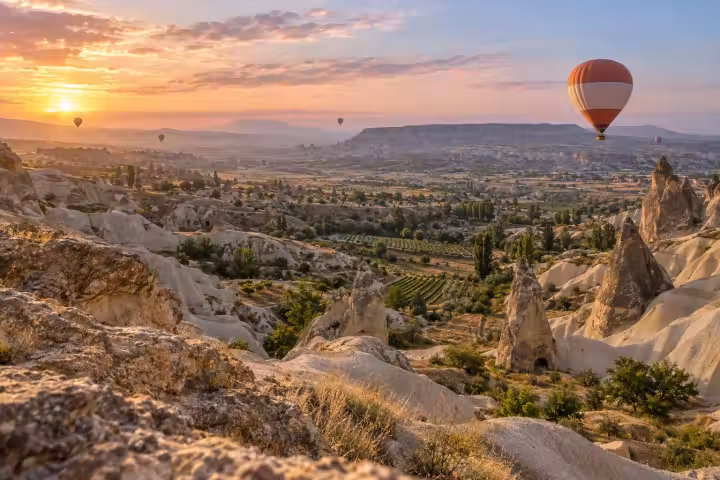 Coral and white balloon above Cappadocia’s vineyards and fairy chimneys at sunrise