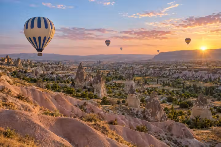 Blue and cream balloon above Cappadocia’s pink ridges and fairy chimneys at dawn
