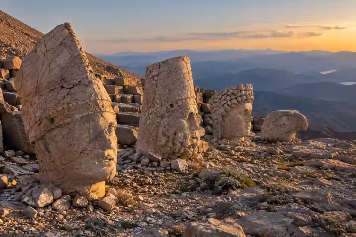 Weathered stone heads on Mount Nemrut above layered mountains in warm evening light