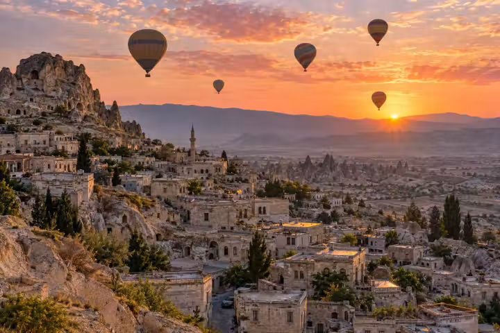 Sunrise hot air balloons above stone houses and rock-cut dwellings in Cappadocia