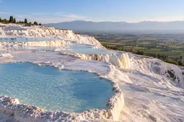 Shallow blue travertine pools above the green plain at Pamukkale in morning light