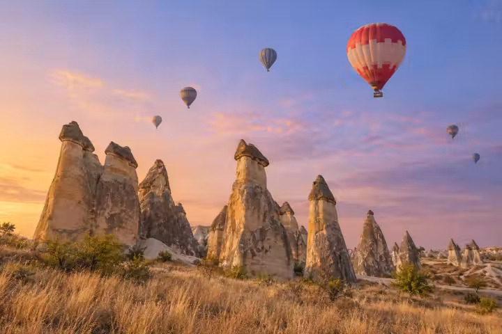 Sunrise balloons above sculpted fairy chimneys and golden grasses in Cappadocia
