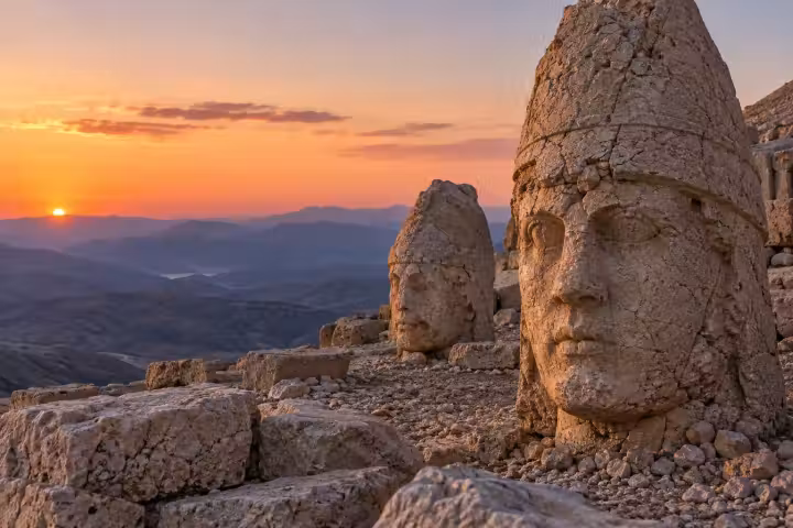 Ancient stone heads on Mount Nemrut with sunrise over distant mountain ridges