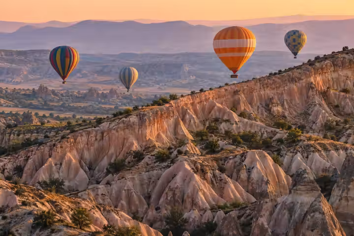 Hot air balloons beyond a rose-colored Cappadocia ridge in warm sunrise light