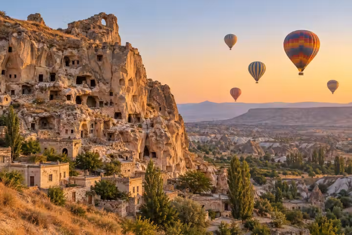 Sunrise hot air balloons beside the rock-cut village cliffs of Cavusin in Cappadocia