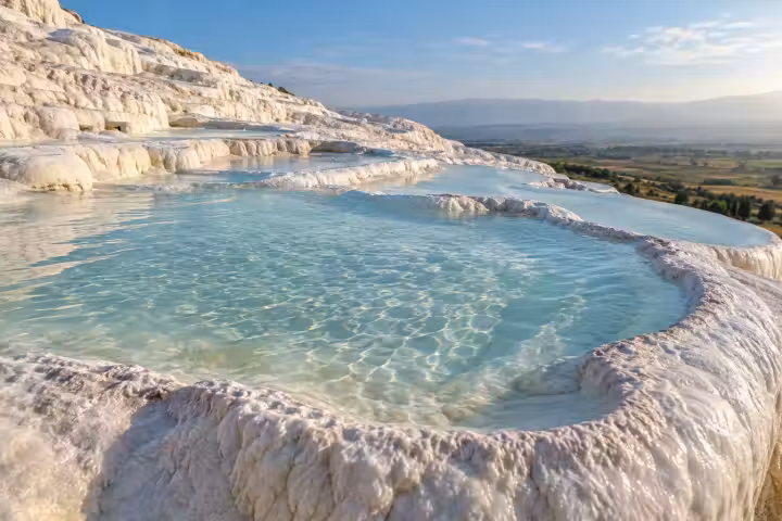 Shallow turquoise water and curved white travertine rims at Pamukkale in morning light
