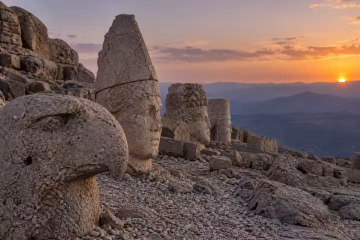 Weathered eagle and human stone heads on Mount Nemrut with mountain views at sunset