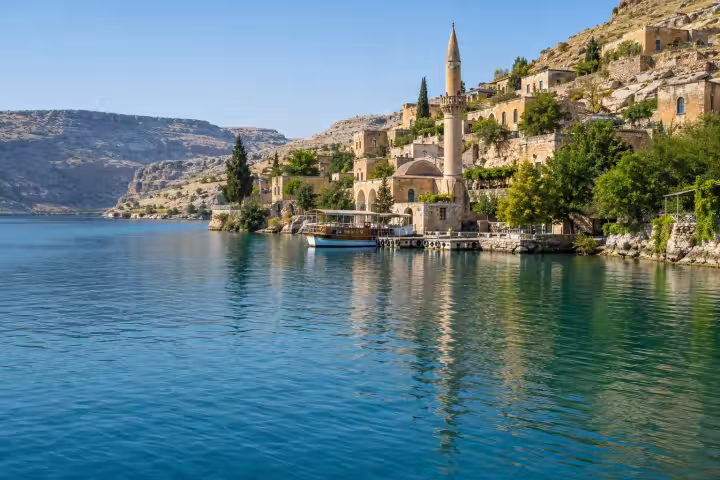 Stone houses and a moored excursion boat beside the blue Euphrates reservoir at Halfeti