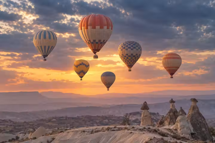 Hot air balloons lit by sunrise beneath textured clouds above Cappadocia fairy chimneys