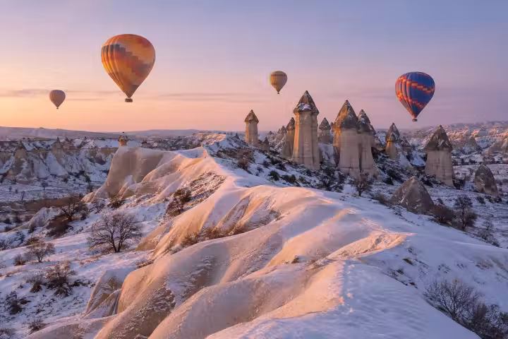Hot air balloons at winter sunrise above snow-dusted Cappadocia ridges and fairy chimneys