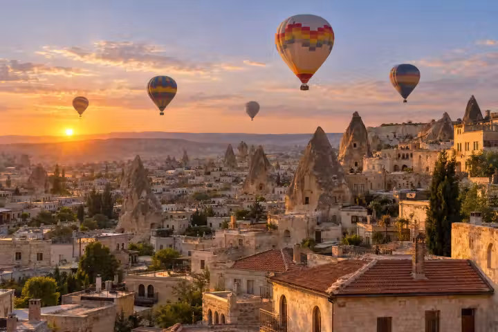 Hot air balloons at sunrise over Goreme cave houses, fairy chimneys and terracotta rooftops in Cappadocia