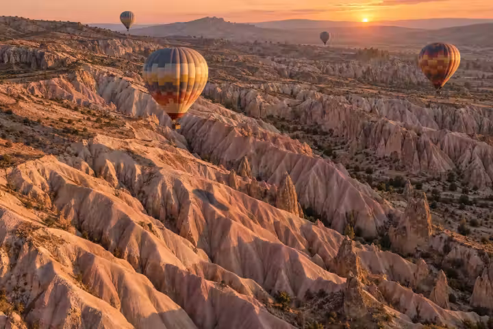 Hot air balloons above Cappadocia’s pink and cream valley ridges at sunrise, seen from an aerial viewpoint