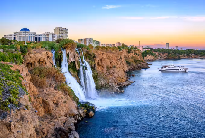Evening colour above the Antalya shore, a passenger ship standing off past the falling water