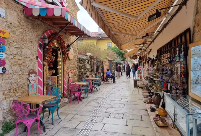 Striped canvas over a narrow Kaleici lane, pink chairs one side and trinket stalls the other