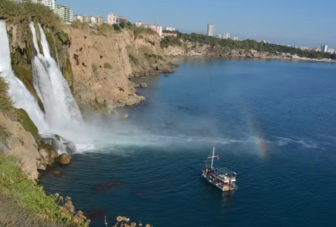 Timber craft holding position right under the Antalya falls, a small bow in the ochre mist