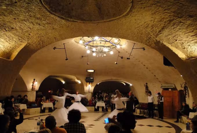 One turning figure alone beneath a hewn cupola, diners seated at their places around it, Cappadocia