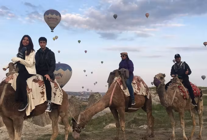Party on dressed mounts along a grassy crest with canopies spread across the sky behind, Cappadocia