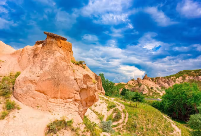 Eroded forms standing out of green ground beneath brilliant piled-up cloud, Cappadocia