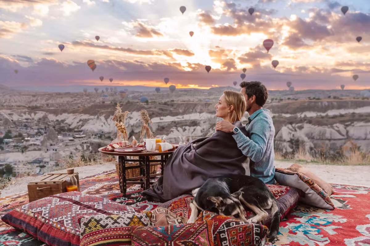 Under one blanket on woven mats at a knee-high board, the fleet lifting off in front, Cappadocia