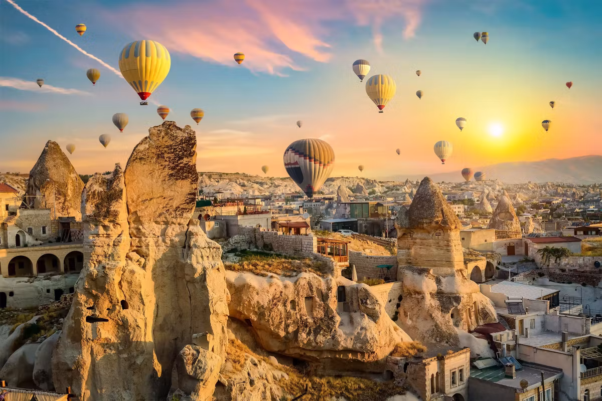 Sun breaking over a cliff full of cut dwellings, envelopes under pink-streaked sky, Cappadocia