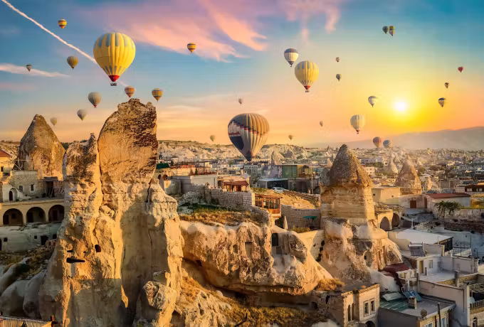 Sun breaking over a cliff full of cut dwellings, envelopes under pink-streaked sky, Cappadocia