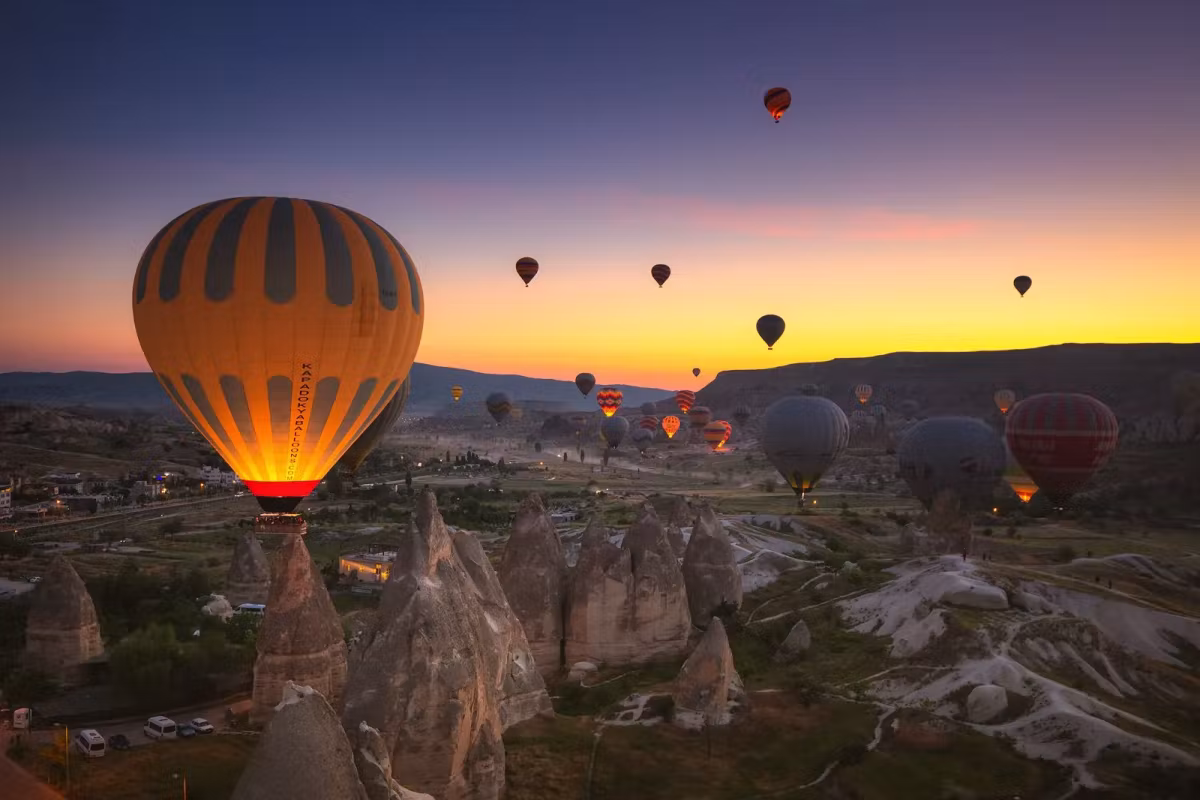 Flame lighting the fabric from inside before daybreak, the spires below still in shadow, Cappadocia