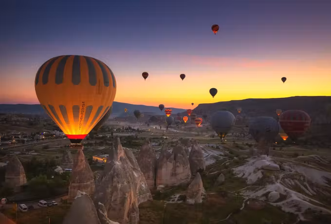 Flame lighting the fabric from inside before daybreak, the spires below still in shadow, Cappadocia