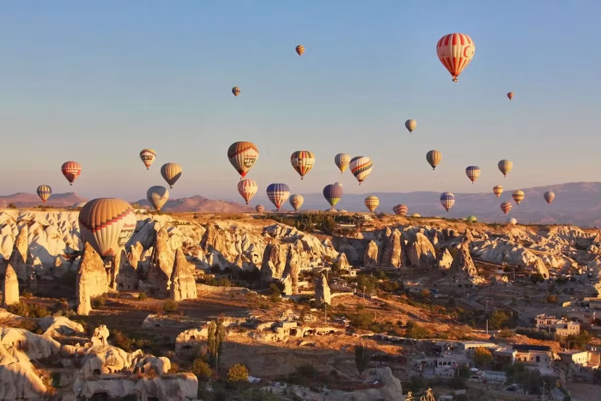 Tight formation passing just above lit tufa and the rooms cut into it, early warmth, Cappadocia