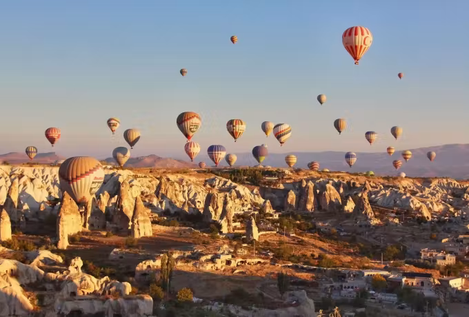 Tight formation passing just above lit tufa and the rooms cut into it, early warmth, Cappadocia