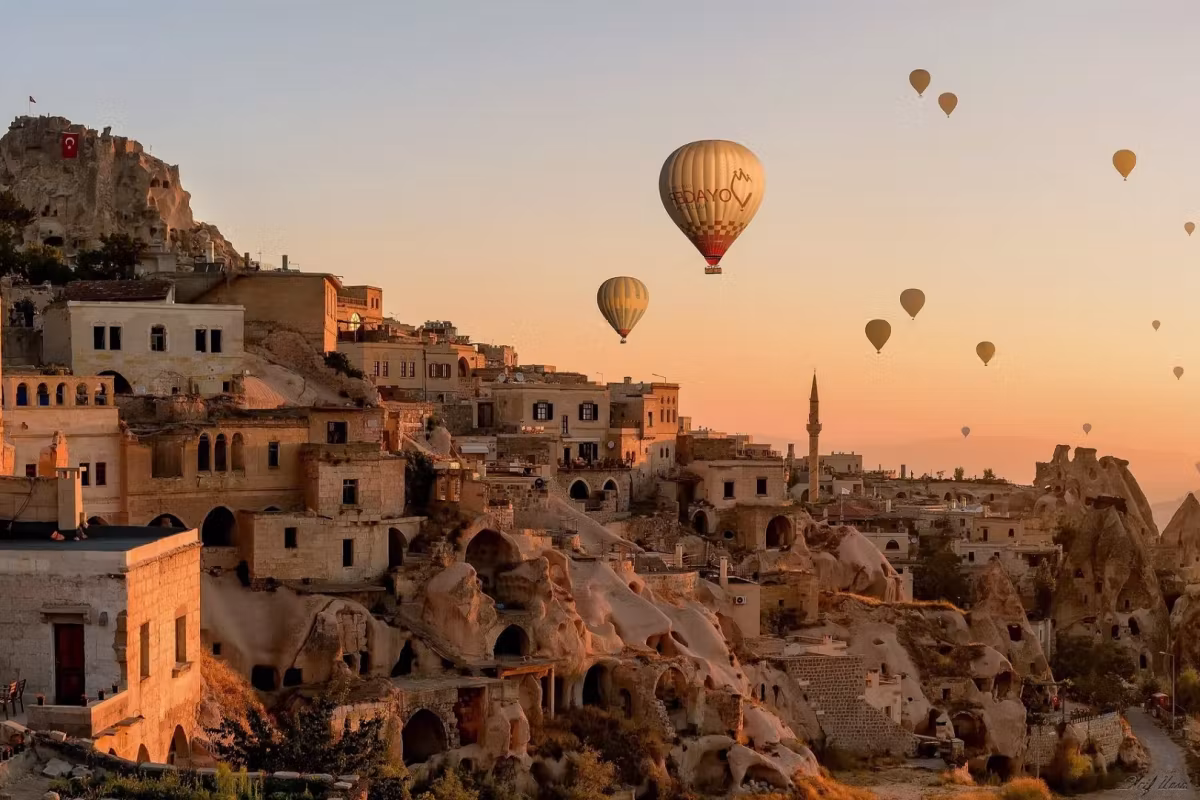 Masonry and cut dwellings stacked up a slope in orange daybreak, a few envelopes beyond, Cappadocia