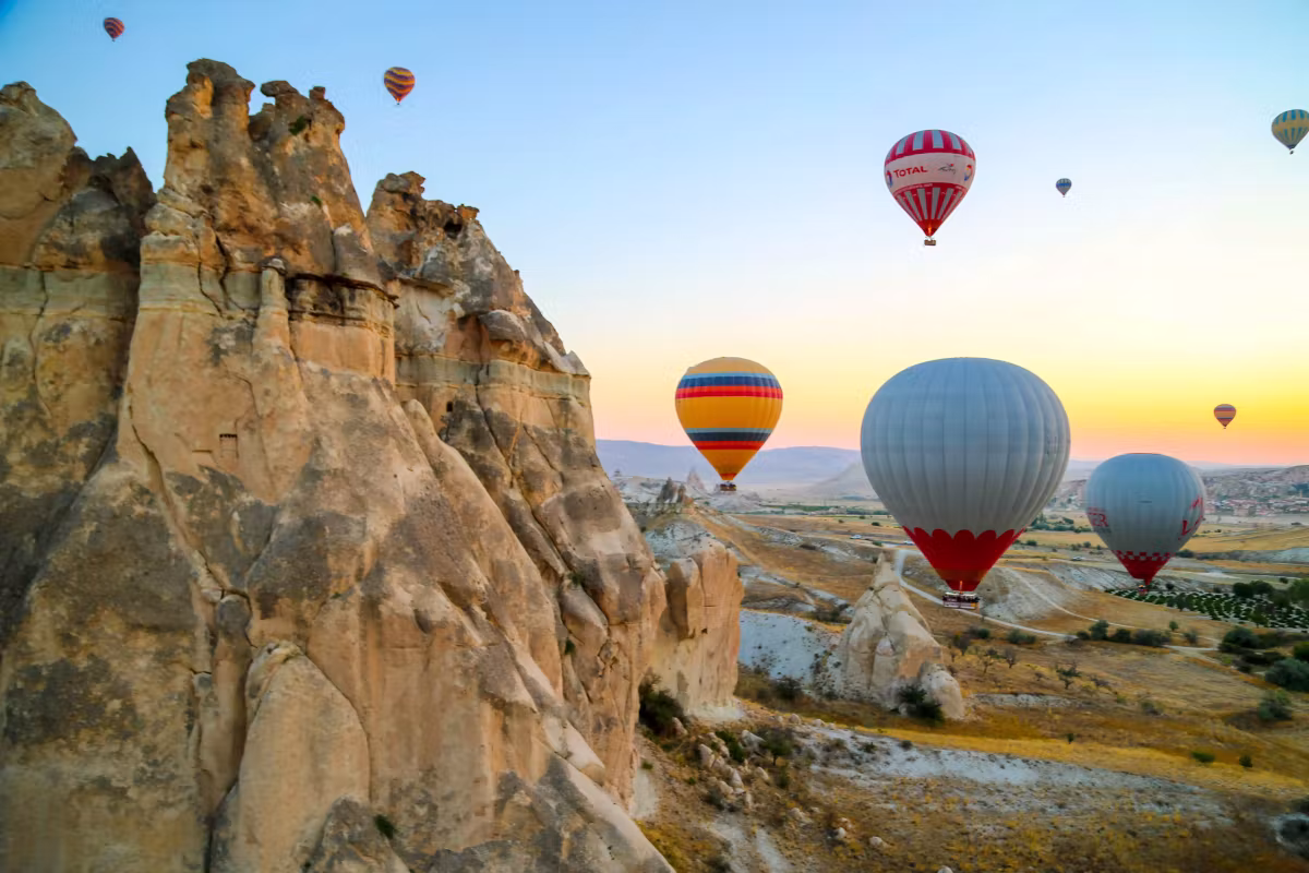 Envelopes brushing past a weathered crag whose edges catch the first sun under clear sky, Cappadocia