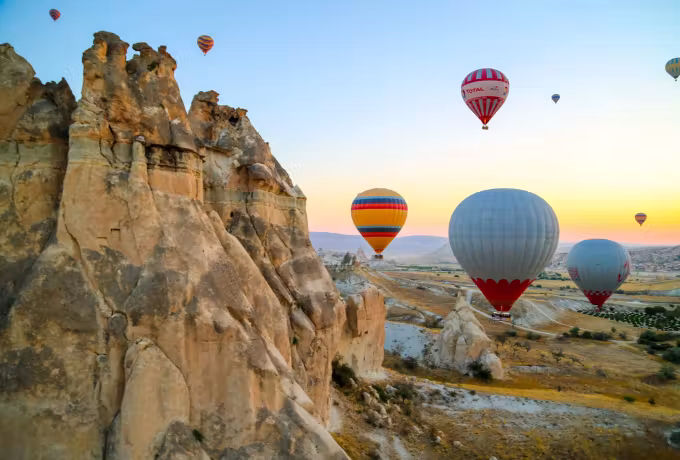 Envelopes brushing past a weathered crag whose edges catch the first sun under clear sky, Cappadocia