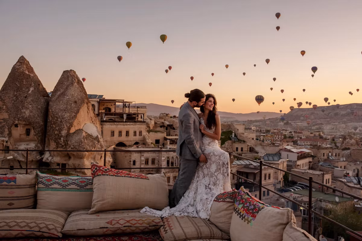 Embrace on a cushioned roof seat with the valley behind full of envelopes in fading light, Cappadocia