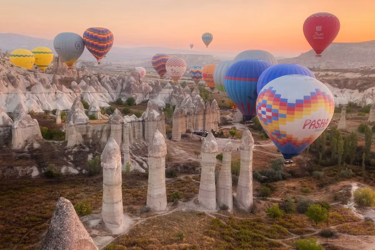 Envelopes crowding the dawn sky over the tall pillars of Love Valley, one passing metres away, Cappadocia