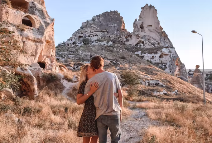 Embrace on a dry hill path with the pitted mass of Uchisar standing straight behind