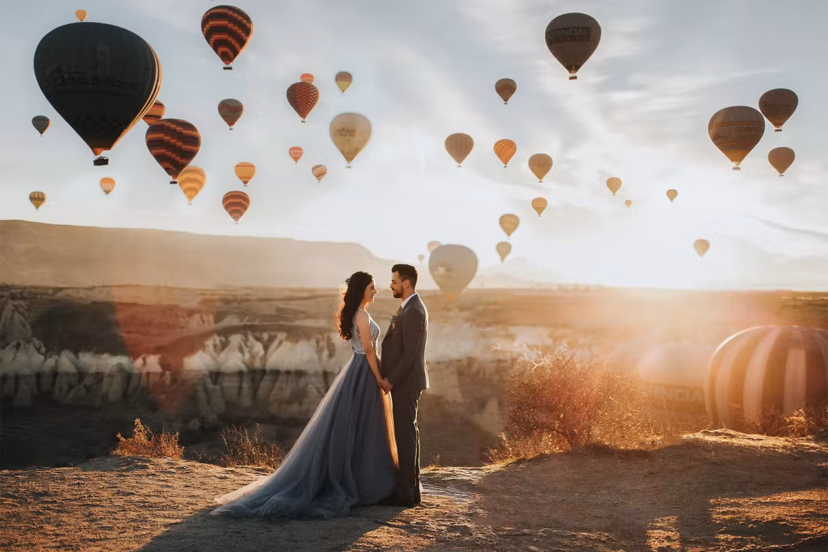 Bridal pair turned face to face on a bare crest at daybreak, envelopes crowding above, Cappadocia