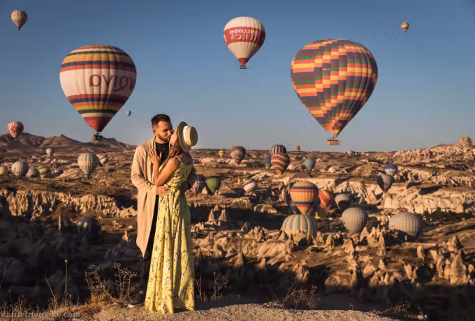 Couple holding each other with two big banded envelopes close behind and dozens far off, Cappadocia