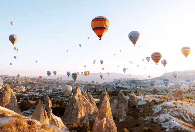 Vivid scarlet and gold fabric nearest the lens, the rest of the flight strung out behind, Cappadocia