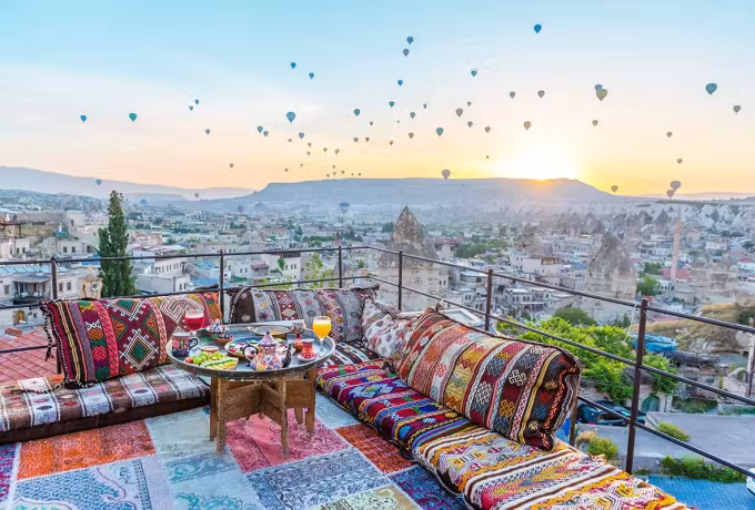 Terrace dressed with woven bolsters and a set board while the basin fills with colour, Cappadocia