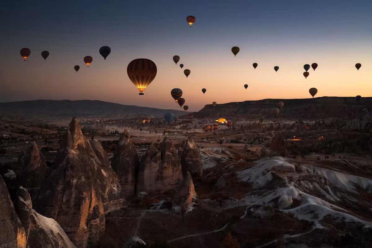 Envelopes climbing in near darkness with only a thin orange band over the black valley, Cappadocia