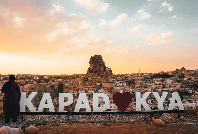 Big Kapadokya lettering at an evening lookout with the Uchisar rock and town behind