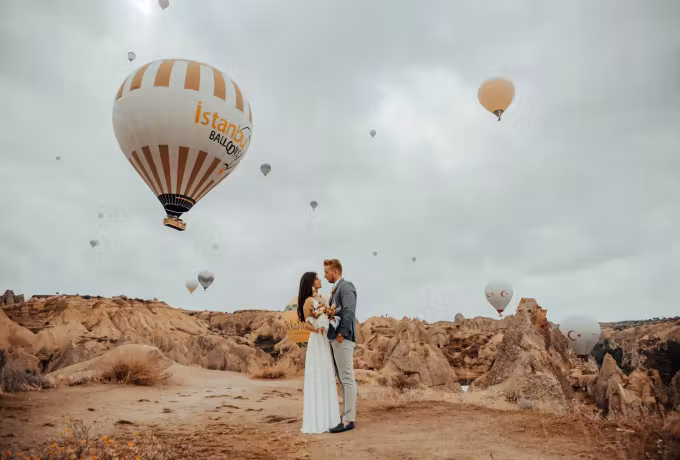 Bridal pair on pale ground with banded fabric drifting low behind them in Cappadocia