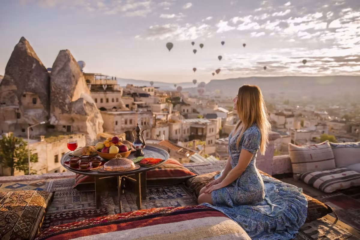 Woman at a dressed board on a woven terrace, carved homes and tufa filling the frame, Cappadocia